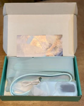 An open teal and white gift box containing a light blue cable, a small white device, and a printed card, photographed on a wooden surface.